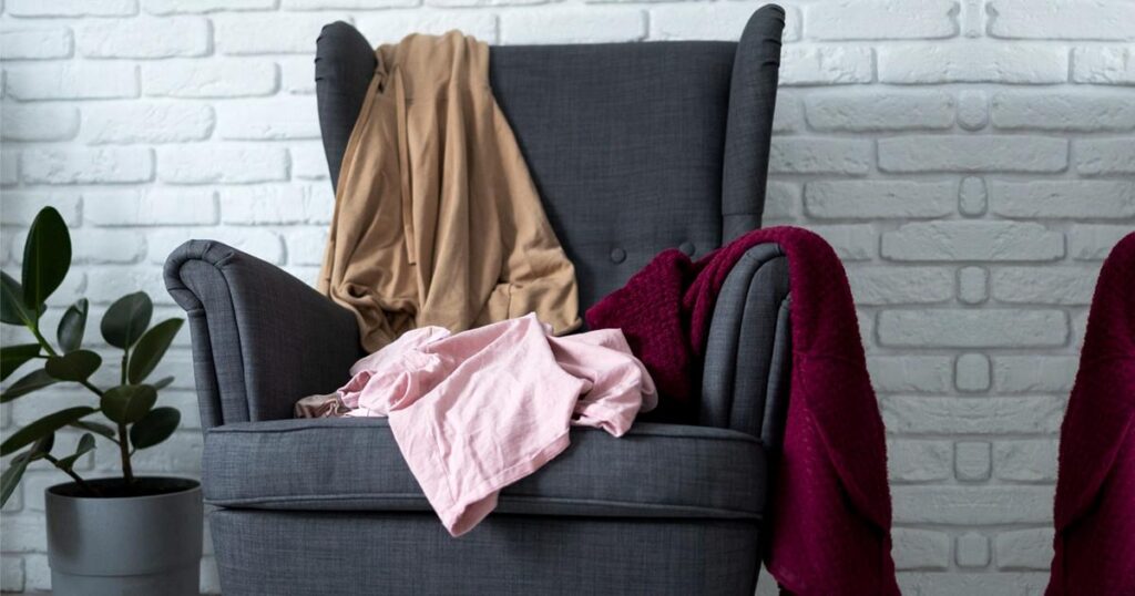A bedroom chair completely covered in a messy pile of jeans and sweaters.