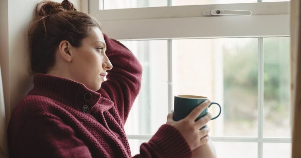 A person looking bored and restless, staring out a window at a snowy landscape.