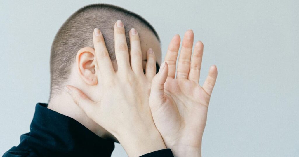 A person covering their face with their hands while someone tries to take a picture of them.