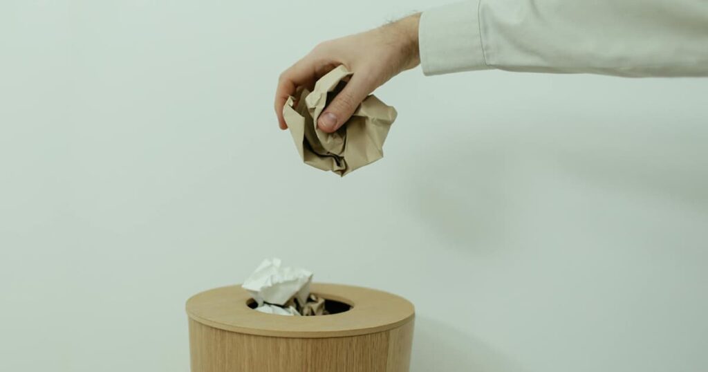 A hand throwing a handful of dried out pens and markers into a trash can.