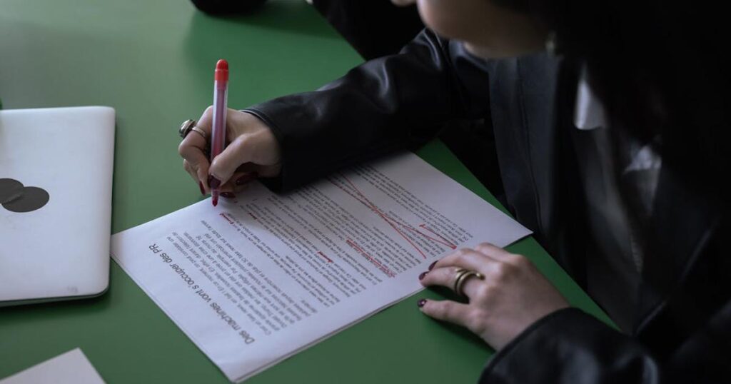 A hand holding a red marker circling items on a printed bank statement.