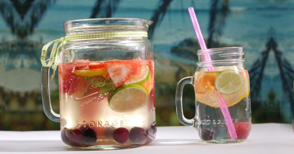 A clear glass pitcher of water filled with slices of lemon, lime, and cucumber.