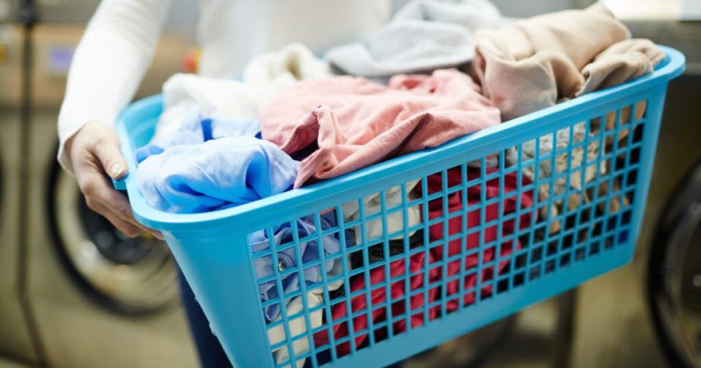 A hand dropping clothes into a laundry hamper, avoiding the floor.