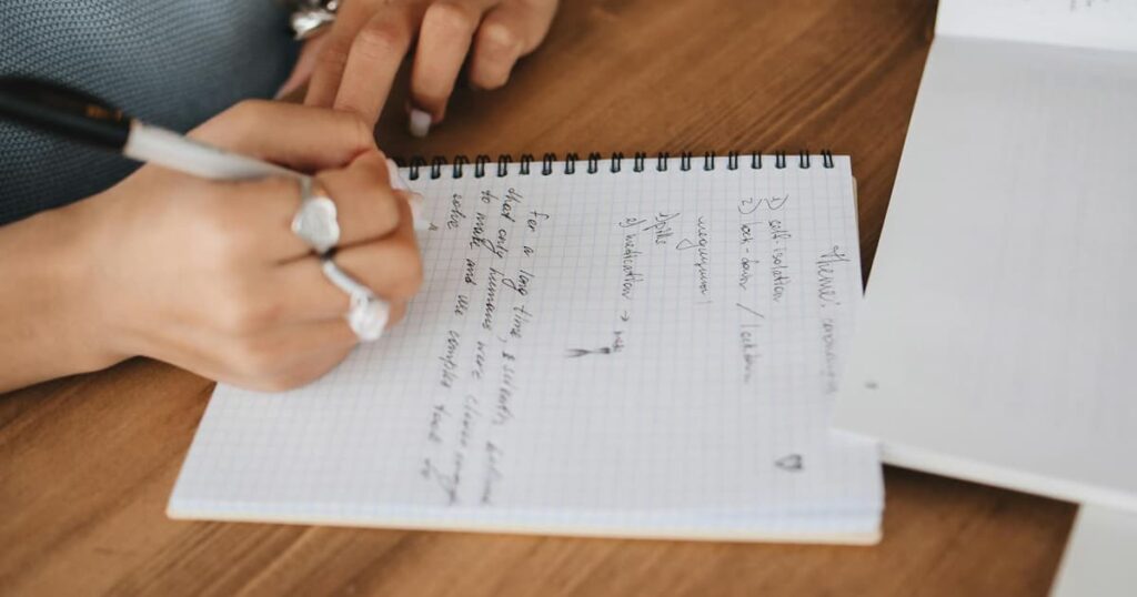 A simple, cheap spiral notebook lying open with messy handwriting inside.