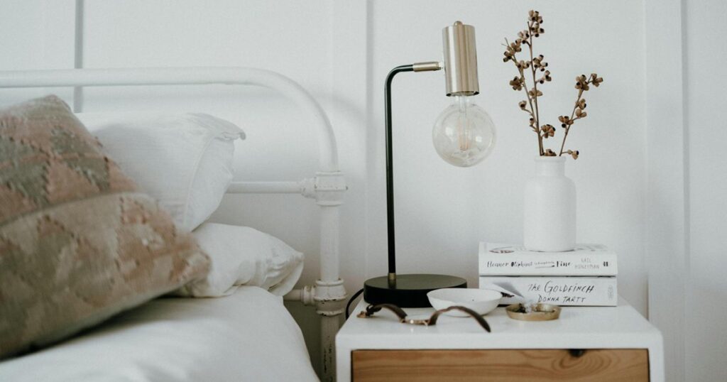 A tidy nightstand with a lamp and book to promote better sleep hygiene.