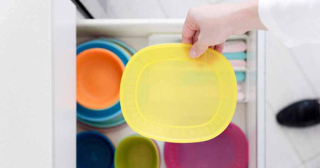 A person holding a round food container and trying to force a square lid onto it.