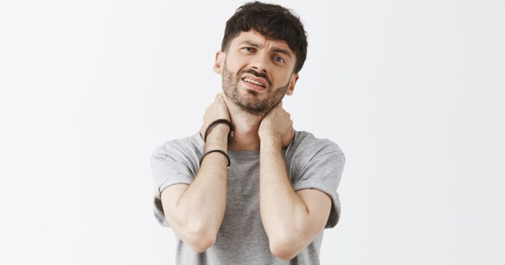 A close up of someone with hunched shoulders and a clenched jaw, showing physical tension.