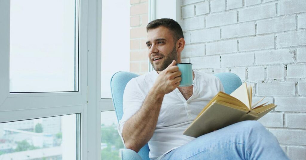 A person sitting alone in a cozy chair reading a book with a cup of tea.