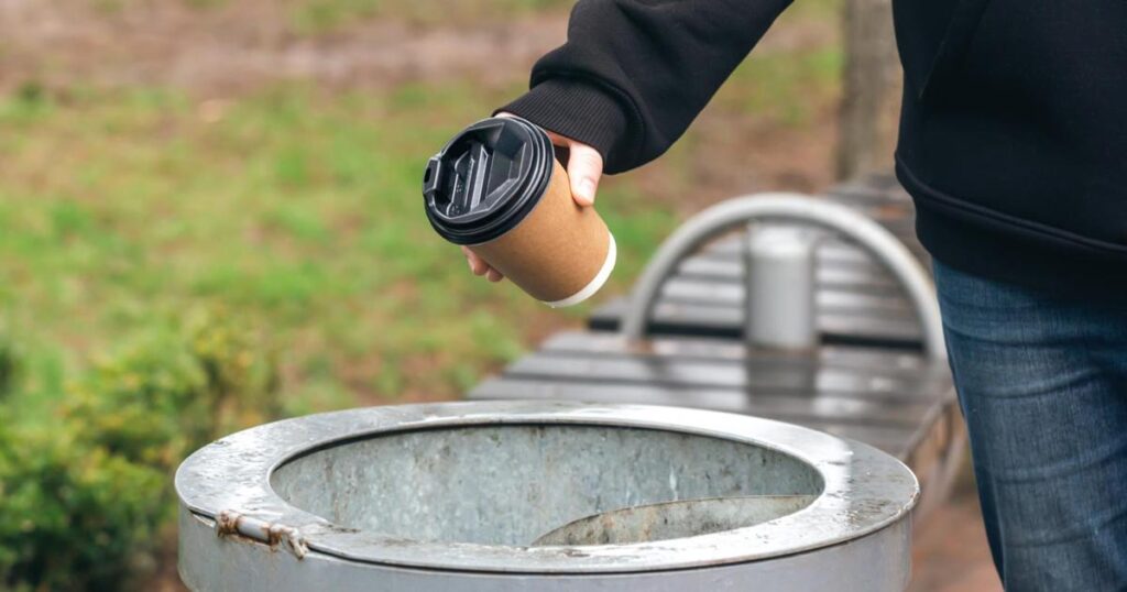 A hand throwing cheap plastic takeout containers into a recycling bin to declutter.