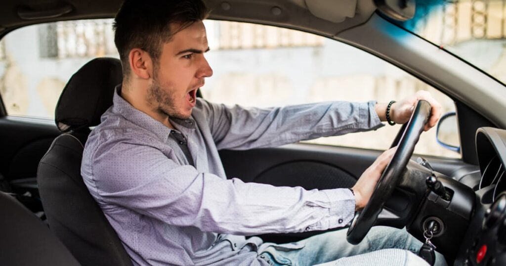 A driver gripping the steering wheel tightly and yelling in frustration.