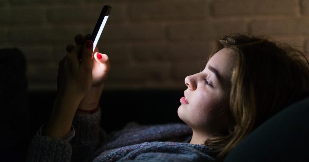 A face glowing from smartphone blue light, representing screen addiction.