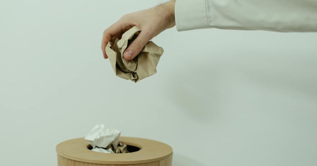 A hand holding a piece of junk mail over a recycling bin, showing immediate decision making.