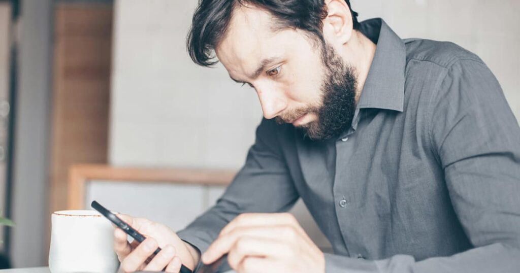 A person looking angry while staring at their phone screen, representing the stress of hate-watching.