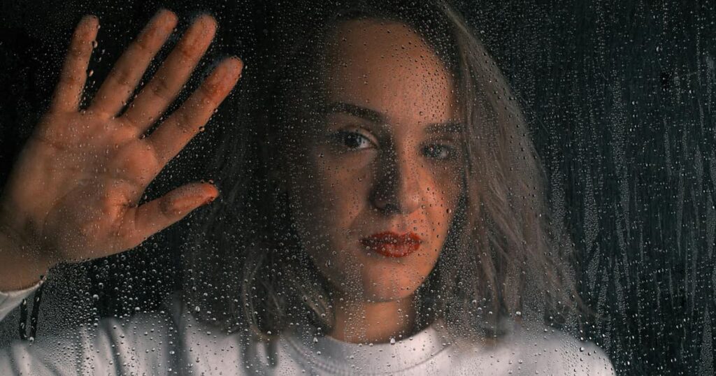 A person looking sadly out a window at a dark, snowy evening, representing seasonal depression.