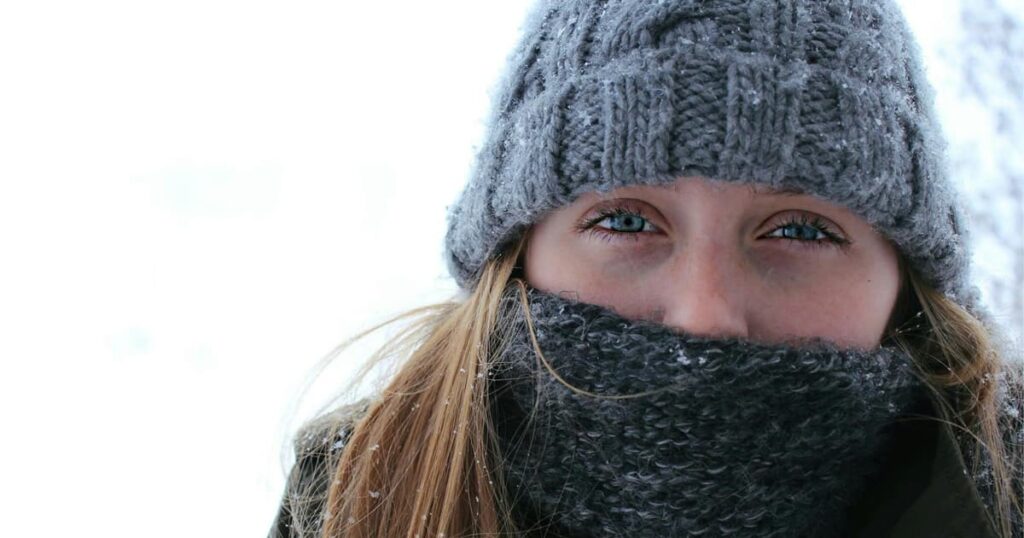 A person bundled up in a coat and scarf walking outside in the snow.