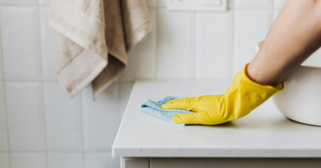 A hand wiping a kitchen counter with a cloth in dim, cozy lighting.