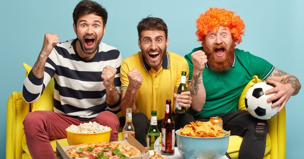 A coffee table filled with simple snacks like chips and dip in front of a TV showing a soccer game.
