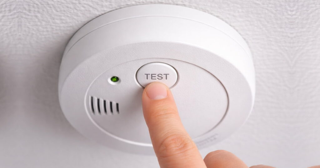 Hand performing a hard reset on a fire detector chirping to stop the low battery noise. You are now 100% ready! 🟢